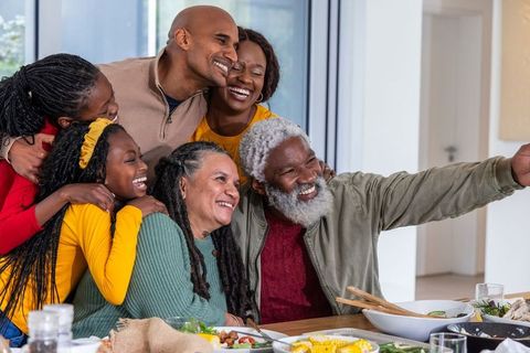 Celebrating multigenerational african american family taking joyful selfie around dinner table