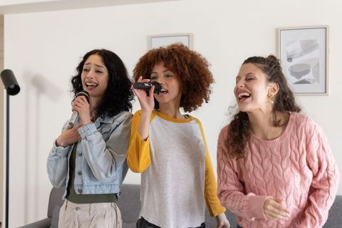 Multiracial friends singing karaoke at home holding microphones laughing and bonding