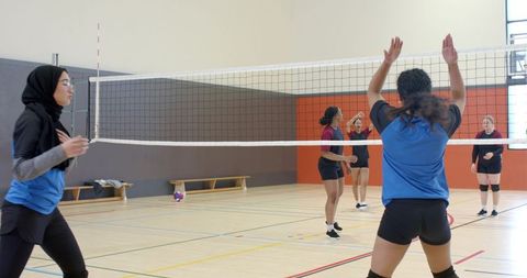 Diverse women's volleyball team wearing hijab and teammates jumping and blocking at net