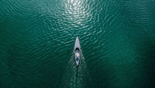 White kayak gliding through turquoise water creating triangular wake and sun reflection