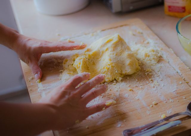 Focus on hands kneading dough on wooden cutting board in kitchen environment. Ideal for cooking blogs, recipes, baking tutorials, food preparation themes, home baking inspirations, and culinary websites.