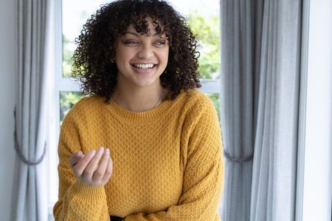 African american woman smiling, gesturing in mustard sweater by window, home portrait