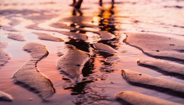 Barefoot couples walking through sunset tide pools on rippling sand with warm reflections