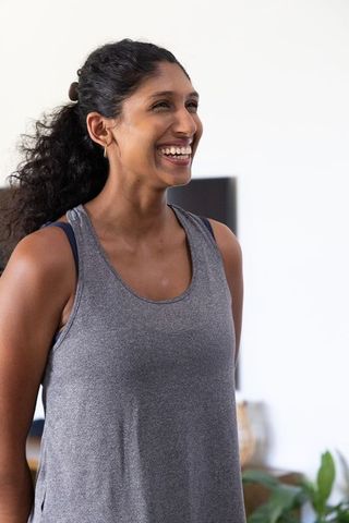 African american woman smiling in sunlit living room wearing gray tank top, hoop earrings