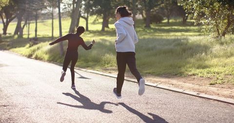 Diverse couple running and jumping on sunlit park path during golden hour