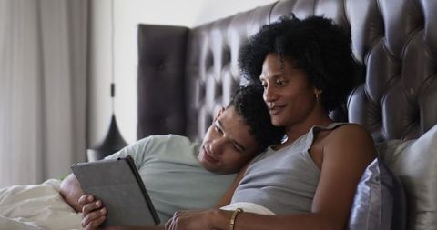 Couple relaxing on bed watching tablet together by tufted headboard, cozy morning routine