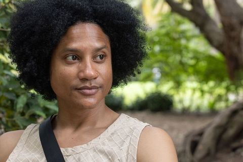 African american man gazing in park wearing sleeveless top and crossbody bag, nose ring, thoughtful