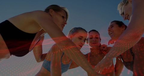 Women huddling outdoors at golden hour wearing activewear with red digital overlay