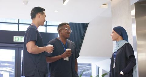 Diverse healthcare team chatting in modern hospital lobby with coffee cups and scrubs