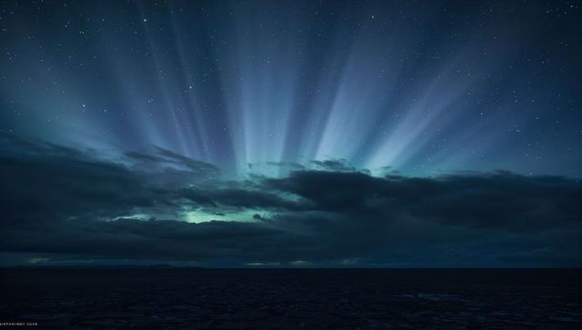 Teal Aurora Rays Over Midnight Sea Dramatic Starry Horizon Light Beams and Glowing Cloud Bank