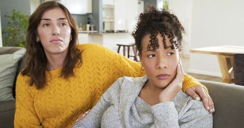 Mixed-race female couple sitting on couch sharing contemplative, supportive moment at home