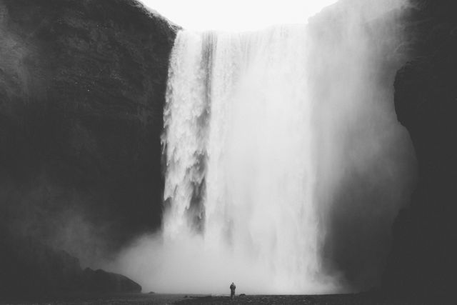 A solitary figure standing in awe before a mighty waterfall, enveloped by mist and natural surroundings. Ideal for themes related to exploration, nature appreciation, adventure, peace, and solitude. Suitable for use in travel blogs, nature documentaries, motivational posters, and environmental conservation campaigns.