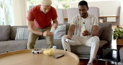 Two friends playing video games and enjoying drinks on modern living room sofa