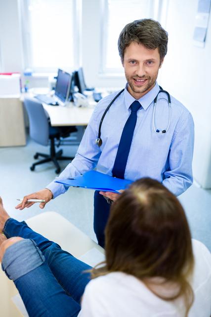 Doctor holding a clipboard, engaging with a patient in a modern clinic office. Suitable for healthcare, medical consultation, patient care, and hospital-themed content. Use this for promoting health services, illustrating patient-doctor interactions, or informing about medical examinations.