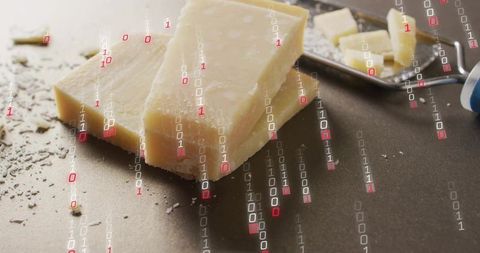 Parmesan wedge sitting on dark counter with shavings and metal plane, binary code overlay