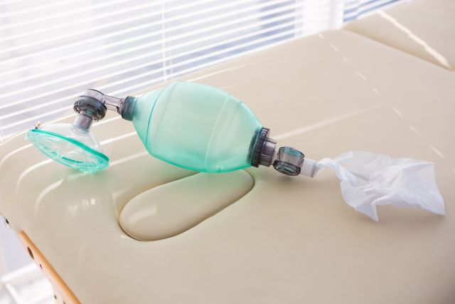 Close-up of an oxygen mask placed on a medical examination table in a clinic. Ideal for use in healthcare-related content, medical articles, emergency response training materials, and hospital brochures.