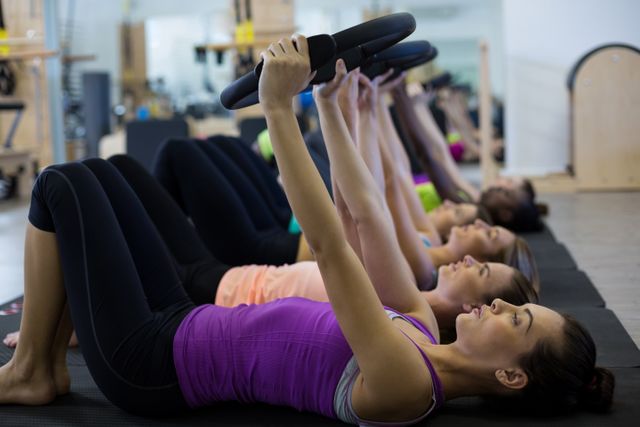 Women participating in a group Pilates class using Pilates rings in a gym. Ideal for promoting fitness classes, gyms, healthy lifestyles, and group workouts. Great for illustrating teamwork, physical fitness, and Pilates training techniques.