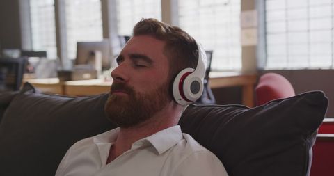Businessman relaxing on office sofa with headphones