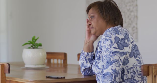 Worried Elderly Woman Seated Next to Phone at Wooden Table - Download Free Stock Images Pikwizard.com