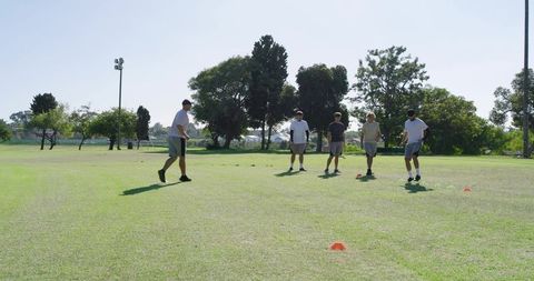 Male teammates training agility drills on sunny grass field weaving cones for fitness