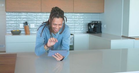 African american man leaning on kitchen island holding tablet smiling by espresso machine