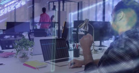 Mid-adult developer coding on laptop in open-plan office with collaborative workspace