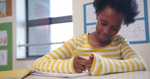 Focused Child Studying with Pencil in Classroom Against Educational Posters