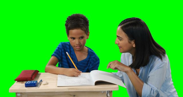 Image shows a teacher tutoring a student at a desk with a bright green screen background. Ideal for educational materials, learning resources, and promotional content for tutoring services. Can also be used for composite work due to the green screen backgound.