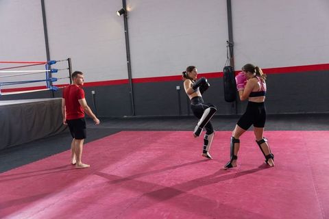 Female kickboxing sparring session with coach on pink mats, blocking kick training
