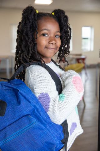 Confident African American Schoolgirl with Blue Backpack in Classroom