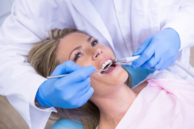High angle view of dentist holding angled mirror while treating woman at medical clinic
