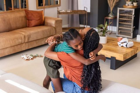 African american mother hugging child on sofa in cozy living room, warm family moment