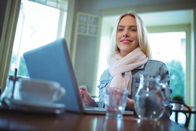Smiling woman using laptop while having coffee - Download Free Stock Photos Pikwizard.com