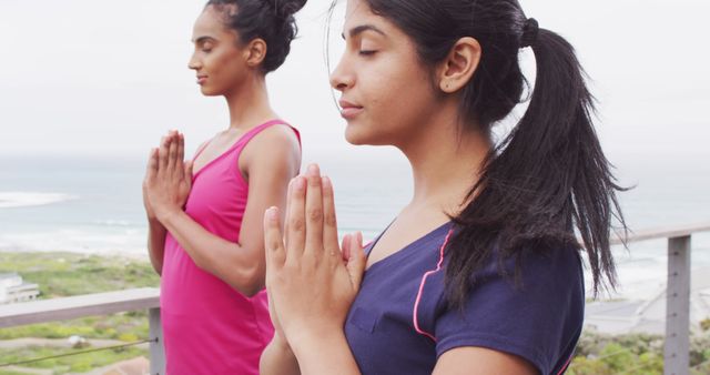 Image of relaxed diverse female friends practicing yoga by sea. Friendship, vacations, spending quality time together.