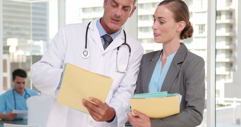 Doctor Discussing Patient Files with Colleague in Modern Office - Download Free Stock Images Pikwizard.com