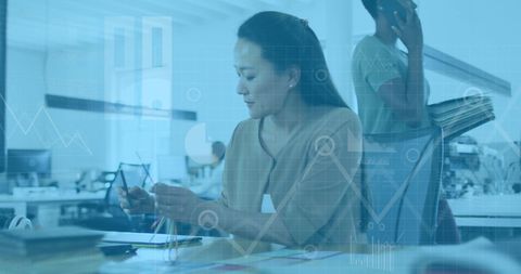 Asian woman analyzing data with digital graphics overlay in modern office