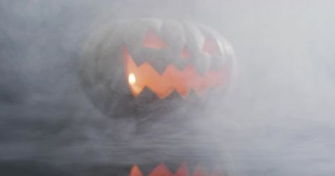 Glowing jack-o-lantern emerging through fog, candlelight reflection on surface