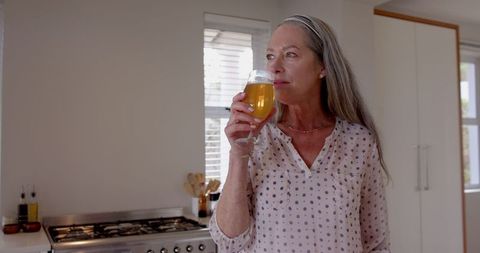 Mature Woman Enjoying Refreshing Beverage in Modern Kitchen