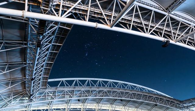 Curved steel trusses framing starlit sky at modern stadium, highlighting metal geometry
