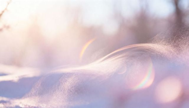 Soft sunrise snow drift curling over frosty meadow with pastel lens flares and bokeh