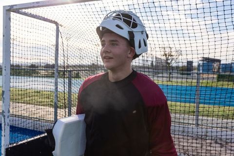 Teen hockey goalie posing confidently with equipment on sports field