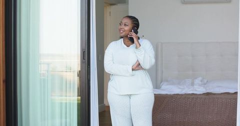 Mid adult african american woman in loungewear standing in doorway talking on smartphone