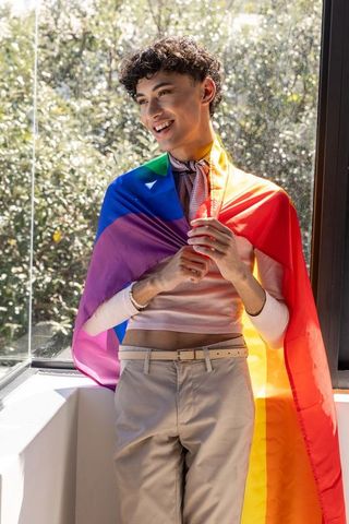 Smiling Man Draped in Pride Flag Embracing Sunlit Interior Moment