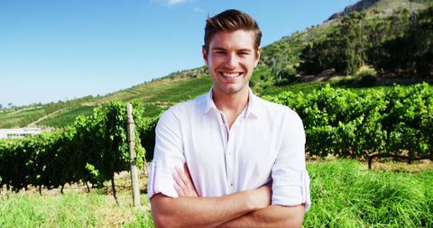 Smiling Man Standing in Sunlit Vineyard with Arms Crossed