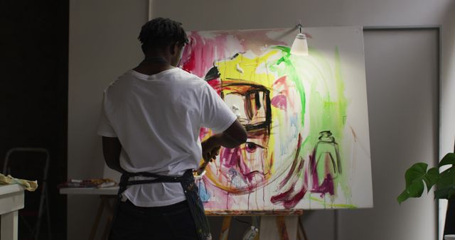 Rear view of african american male artist wearing apron painting on canvas at art studio. art, hobby and creative occupation concept