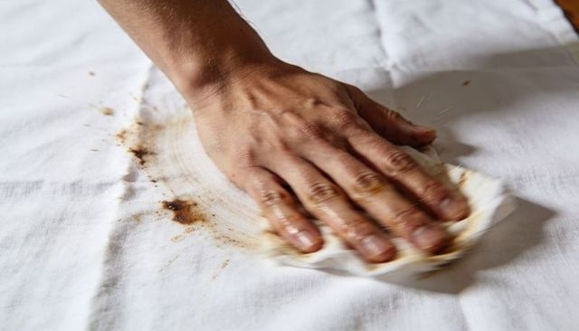 Hand wiping grease stain on white tablecloth with paper towel
