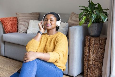 African american woman relaxing with headphones on living room floor, cozy home wellness