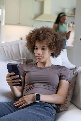 African american women relaxing on sofa using smartphone and smartwatch in modern home