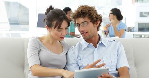 Colleagues Collaborating on Tablet in Modern Office Lounge