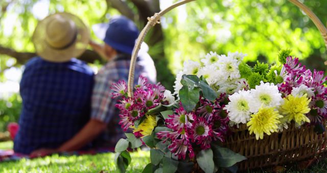 A basket full of vibrant flowers sits in the foreground with a senior Caucasian couple enjoying a peaceful moment in a lush garden, with copy space. Their relaxed posture and casual attire suggest a serene retirement lifestyle or a leisurely weekend outing.